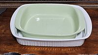 Green rectangular Chantal casserole dish placed inside larger white CorningWare casserole dish on a wooden surface.