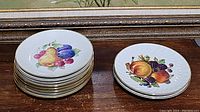 Stack of 8 gold rimmed fruit plates with colorful fruit painting and 2 smaller plates with different fruit designs