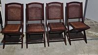 Front view of set of 4 dark wood folding chairs with cane seats and backs, arranged side by side.