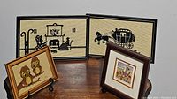 Four framed artworks on a wooden surface, showing distinct cross stitch and illustrated styles