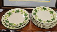 Two stacks of ivory plates with green ivy patterns on the rim, 6 smaller dinner plates on the right and 2 larger serving plates on the left.