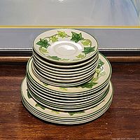 Stack of multiple plates showing the full range of sizes and styles in the set, illustrating the ivy pattern and green rims.