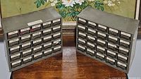 Photo showing two gray metal compartment bins with many small labeled drawers filled with hardware pieces