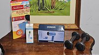 Photo showing all four items: Sunbeam heating pad box, Sanpu digital thermometer box, Conair compact hair dryer boxed, pair of black metal dumbbells.