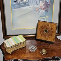 Overview of all items including gold tone jewelry box, glass flower trinket box, glass ring holder, and wood wall plaque in front of framed artwork.