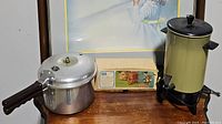 Overview photo showing aluminum pressure cooker, boxed food chopper, and avocado green vintage coffee maker on wooden table.