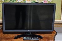 Front view of LG 22" HD smart LED TV on stand with remote in front