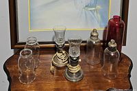 Photo of the vintage lamps, lamp chimneys, and hurricane shades arranged on a wooden surface.