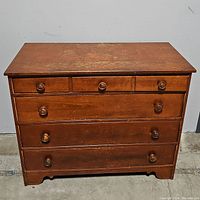 Front view of the oak dresser showing four drawers and round wooden knobs. Visible wear on the surface.