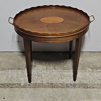 Full front view of the oval mahogany tea table showing scalloped edges and brass handles.