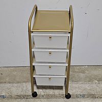 Front view of rolling storage cart showing four clear drawers with gold knobs and gold metal frame
