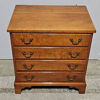 Front view of wooden chest with four drawers, brass handles, and base bracket feet.