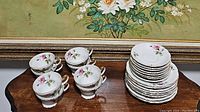 Photo showing 5 teacups stacked next to stacks of 8 saucers and 8 plates, all with floral patterns and gold trim.