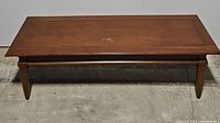 Front view of mid century style wood coffee table showing rectangular top, tapered legs, and wood finish.