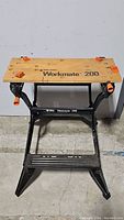 Full view of Black and Decker Workmate 200 folding workbench showing wooden top with orange clamp jaws and black metal frame.
