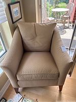 Front view of full beige upholstered arm chair with wooden legs
