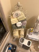 Photo of decorative towel rack with assorted towels, humidifier, and paper towels on a holder.