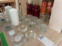 Overview of white pillar candles, clear faceted votive holders, and red glass votive holders on a dresser with mirror behind.