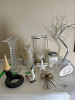Overview of decorative candle holders, hurricane lamp, fibre-optic tree, angel snow globe, napkin holder, and figurines arranged on a white surface against a beige wall.