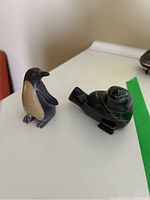 Photo showing the penguin and seal soapstone figurines placed on a white surface, viewed from the front angle, highlighting their size and color.