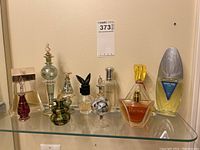 Full set of 11 collectible perfume bottles of various styles and sizes on a glass shelf, showing variety of shaped bottles including hand painted and decorative features.