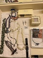 Full overview of lot showing various necklaces, earrings, watch, small jewelry boxes and bracelets spread on a white cloth