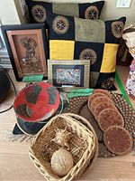 Photo showing two geometric patterned pillows, two framed artworks (one Indonesian, one aboriginal), red and black wicker basket, small wicker basket with ornaments, leather coasters and large woven platter.