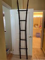 Full view of tall handcrafted rattan ladder leaning against a white door in an indoor space.