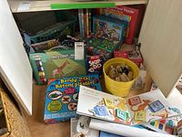 Puzzles with games, painting kit, wooden blocks in yellow bucket, alphabet cards, books, and DVDs in shelf space.