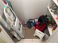 Photo showing ironing board and folding step stool with some cleaning and utility items in corner of room.