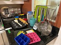Wide view showing countertop with various kitchen bakeware, mixing bowls, utensil rack, and silicone molds