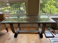 Photo showing front view of the coffee table with metal frame and clear glass top in front of window.