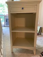 Front view of the white nightstand showing the single drawer with square metal knob and two open shelves below.