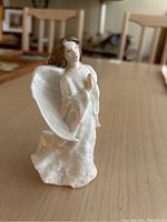 Porcelain Christmas angel figurine with white wings, brown hair, and white flowing gown, viewed from angle showing front half and clasped hands.