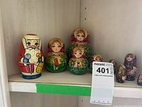 Eight Russian nesting dolls displayed on wooden shelf, including a Santa Claus figure and seven traditional female dolls with colorful scarves and folk patterns.