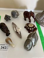Photo showing variety of animal carvings including wooden elephant, hippopotamus, wooden turtle with coasters, soapstone face, small carved birds and metal bird.
