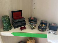 Overview of several small hand painted boxes and two figurines arranged on shelf