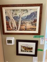Two framed watercolours hung on a wall, one large landscape painting signed as style of Albert Namatjira, another smaller painting of a cow signed Ros 2013.