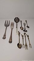 Full set of 10 serving utensils arranged in two rows showing a variety of forks and spoons with both mother-of-pearl and metal ornate handles