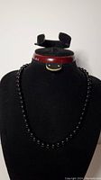 Black glass bead necklace displayed on a black neck form showing the full length and arrangement of beads.