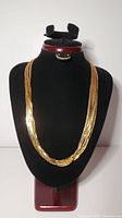 Full view of the gold-coloured necklace displayed on a black neck form, showing 10 strands and wide clasp.