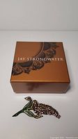 Jay Strongwater branded brown box with lace design, brooch placed in front