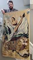 Full view of man holding Moulin Rouge tapestry showing can-can dancer and colorful vintage poster art.