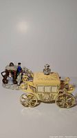 Image of cream and gold coloured musical carriage jewellery box with ceramic figure behind it.