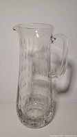 Full view of tall clear glass pitcher with stretch bubble pattern and attached handle