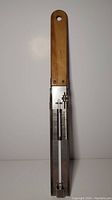 Full view of vintage candy thermometer with wooden handle and metal body showing thermometer tube