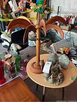 Photo of wooden palm tree statue with large curved fronds and small wooden snail at base, set on round table with other figurines