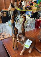 Three wooden animal figurines on a wooden table including an elephant and two giraffes in the background, surrounded by glassware.