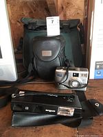 Photo of Argus Carefree 110F film camera with strap and case, HP Photosmart 735 digital camera, and black camcorder partially visible behind them.