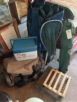 Photo showing three blue and green folding lawn chairs in carrying cases, Thermos cooler tote, fishing net, and wooden slatted plant stands on caster wheels